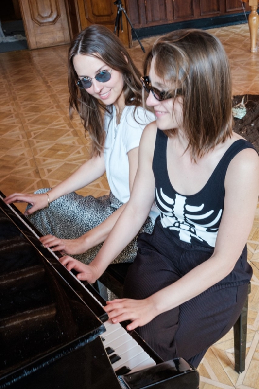 dwie młode, uśmiechnięte kobiety grają na fortepianie