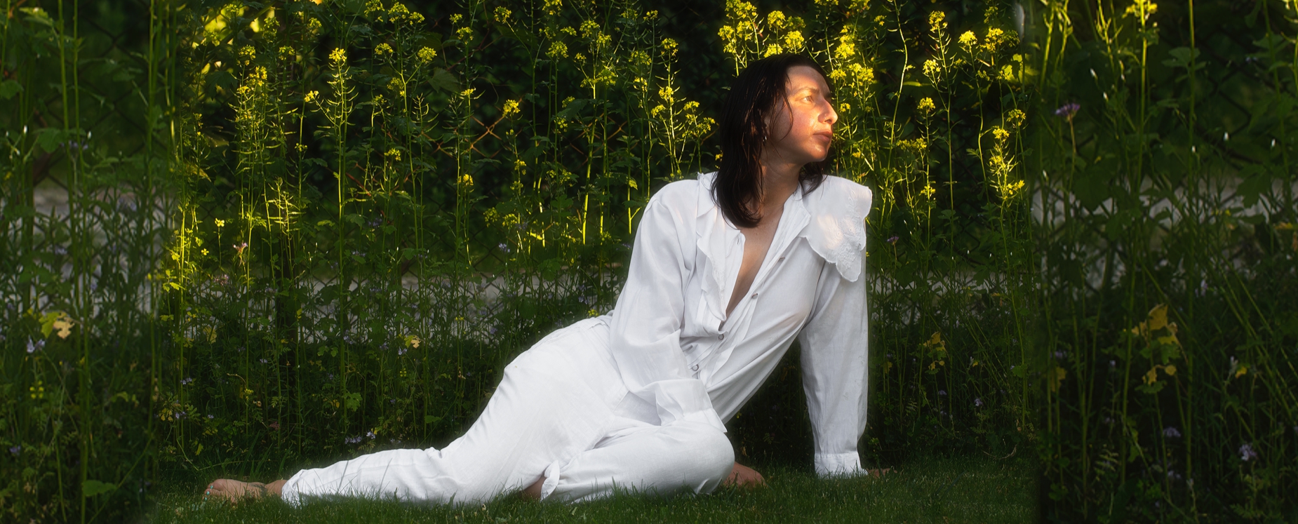 Na zdjęciu Antonina Nowacka. Zdjęcie osoba w białym ubiorze siedzi na trawie w tle zieleń drzew i krzewów.
