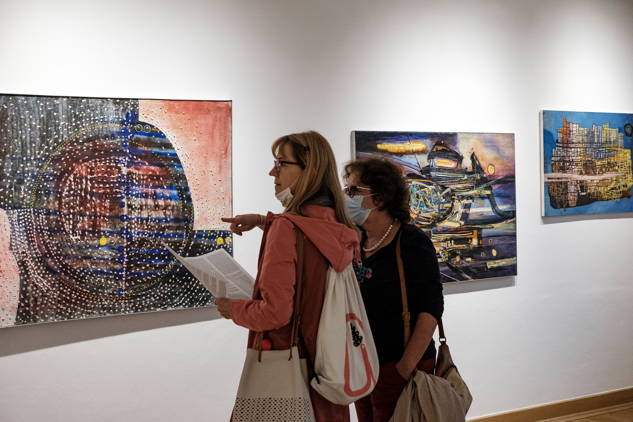 Ilustracja dekoracyjna. Dwie kobiety oglądaja obrazy Mariana Bogusza na wystawie Krzywe Koło.