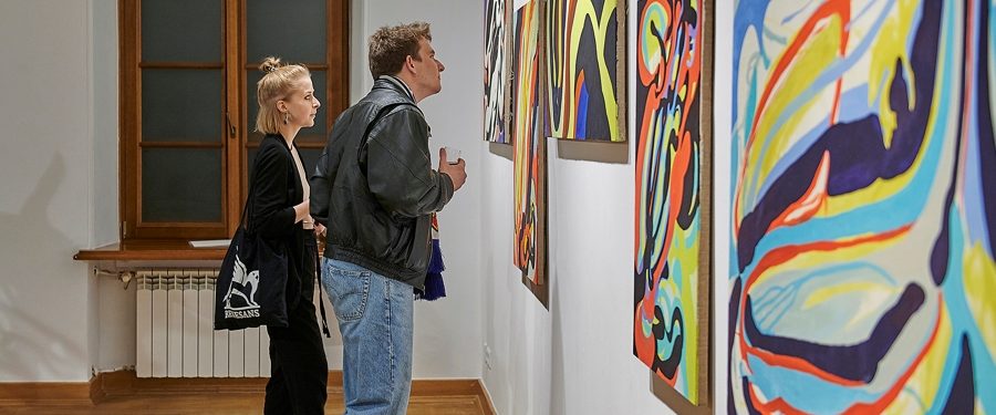 Mężczyzna i kobieta oglądają obrazy na wystawie malarstwa w Galerii Promocyjnej.