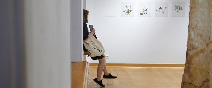 Młoda kobieta siedzi na parapecie w galerii i ogląda wystawę.