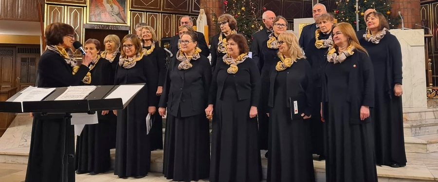 Chórzystki i chórzyści zespołu Jubilus z durygentką, ubrani w czarne stroje, stoją we wnętrzu prezbiterium kościoła.