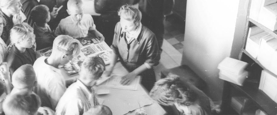 widziane z góry stoisko z książkami i prasą; sprzedawczyni pakuje książkę a wokół stoi grupa młodzieży