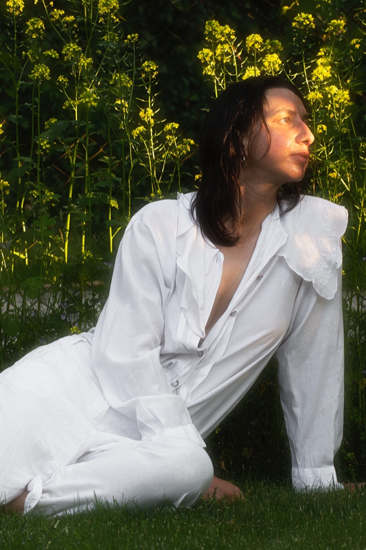 Na zdjęciu Antonina Nowacka. Zdjęcie osoba w białym ubiorze siedzi na trawie w tle zieleń drzew i krzewów.
